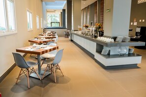 A modern dining area with long tables and chairs, a buffet counter with various food items, and a sign indicating the direction to the bathroom.