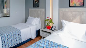 Ein Hotelzimmer mit zwei Betten, einem Nachttisch mit Telefon und Fernbedienungen, einer Zimmerpflanze und Bildern an den Wänden.
