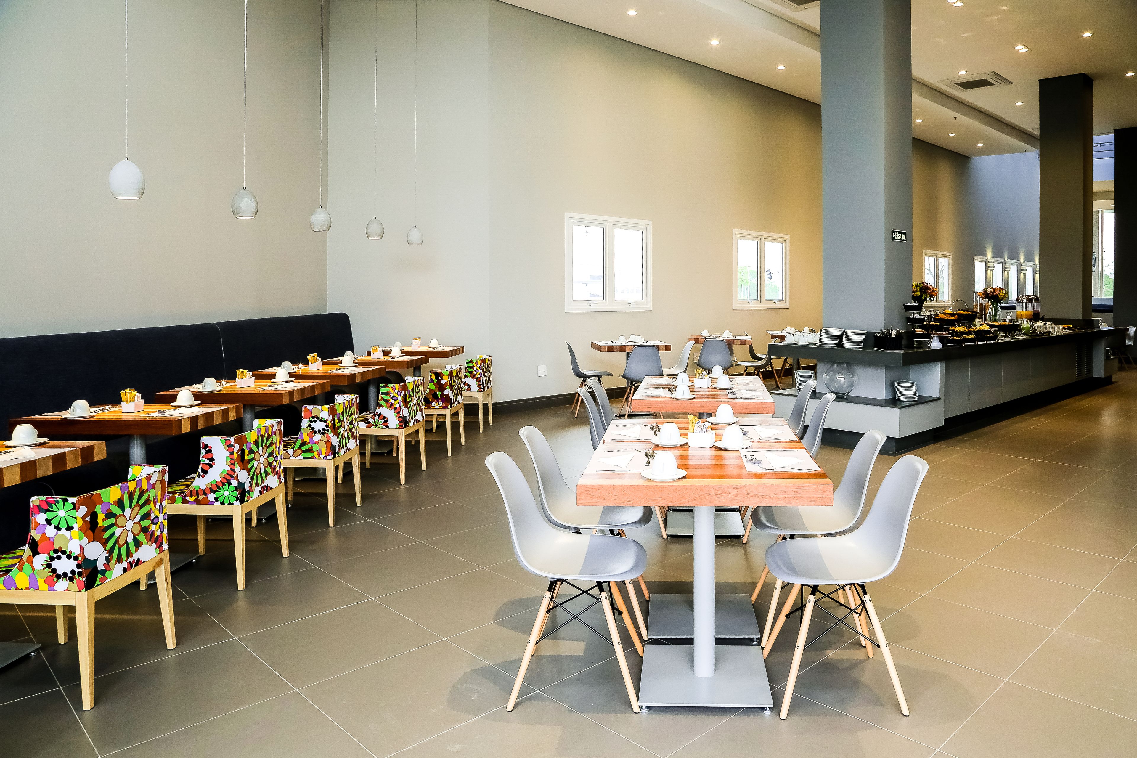 Un vaste espace dédié à la salle à manger, avec de nombreuses tables et chaises, un buffet et de grandes fenêtres qui laissent entrer la lumière naturelle.