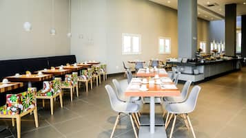 Een ruime eetruimte met meerdere tafels en stoelen, een buffet en grote ramen voor natuurlijk licht.