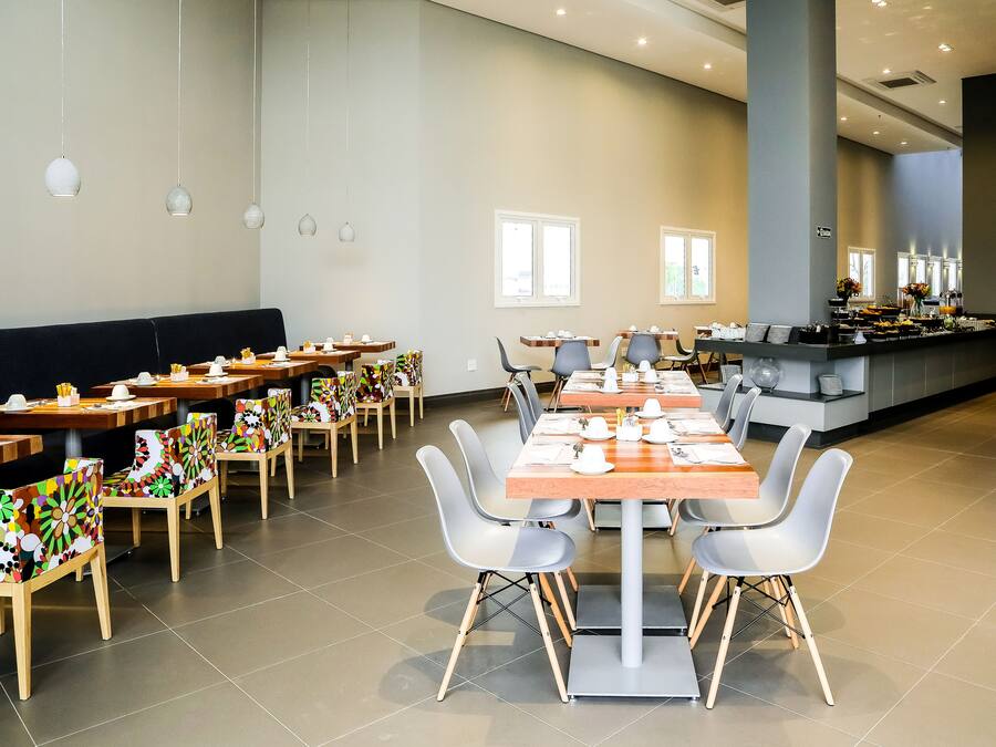 Een ruime eetruimte met meerdere tafels en stoelen, een buffet en grote ramen voor natuurlijk licht.