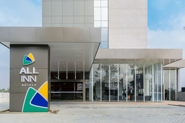 The exterior of an All Inn Hotels building with a modern design, large glass windows, and a prominent logo.