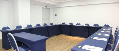 Une salle de conférence avec une longue table, des chaises bleues et des murs blancs.
