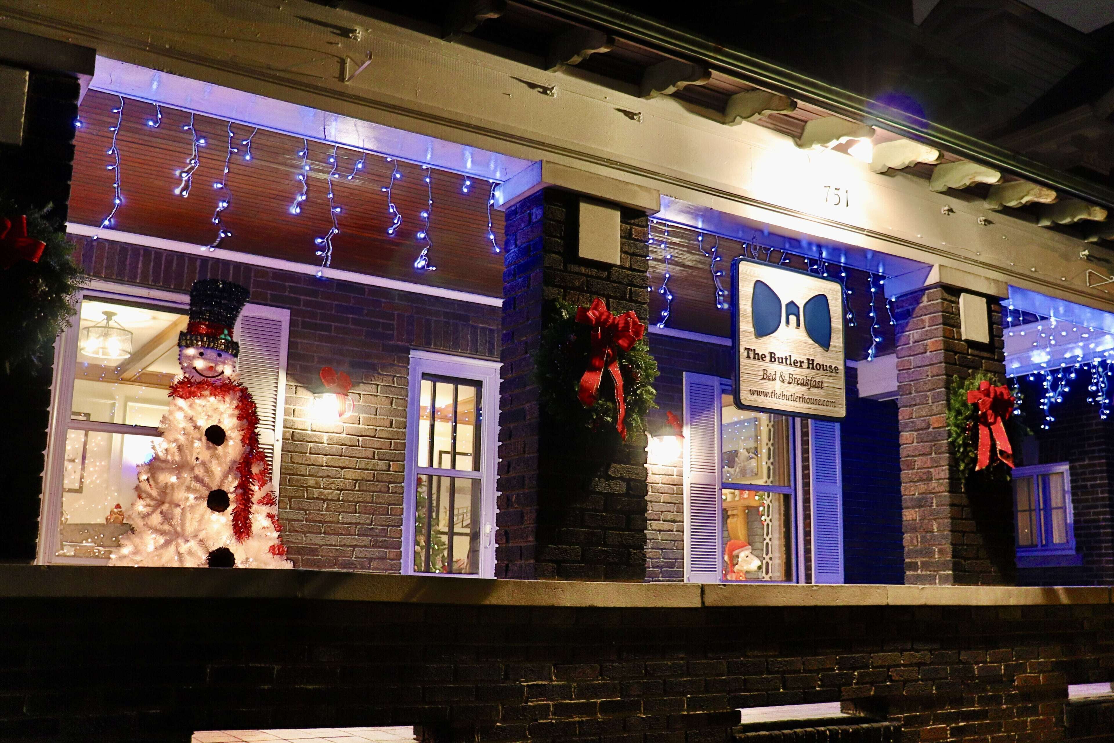 Un edificio con fachada de ladrillo, un letrero que dice 'The Butler House Bed & Breakfast', y decoraciones navideñas, incluyendo un muñeco de nieve y lazos rojos.