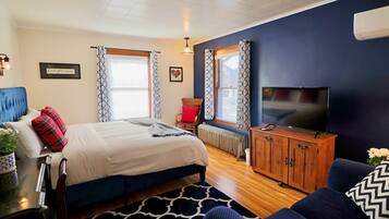 A bedroom with a bed, a TV, a wooden cabinet, a chair, and a window with patterned curtains.