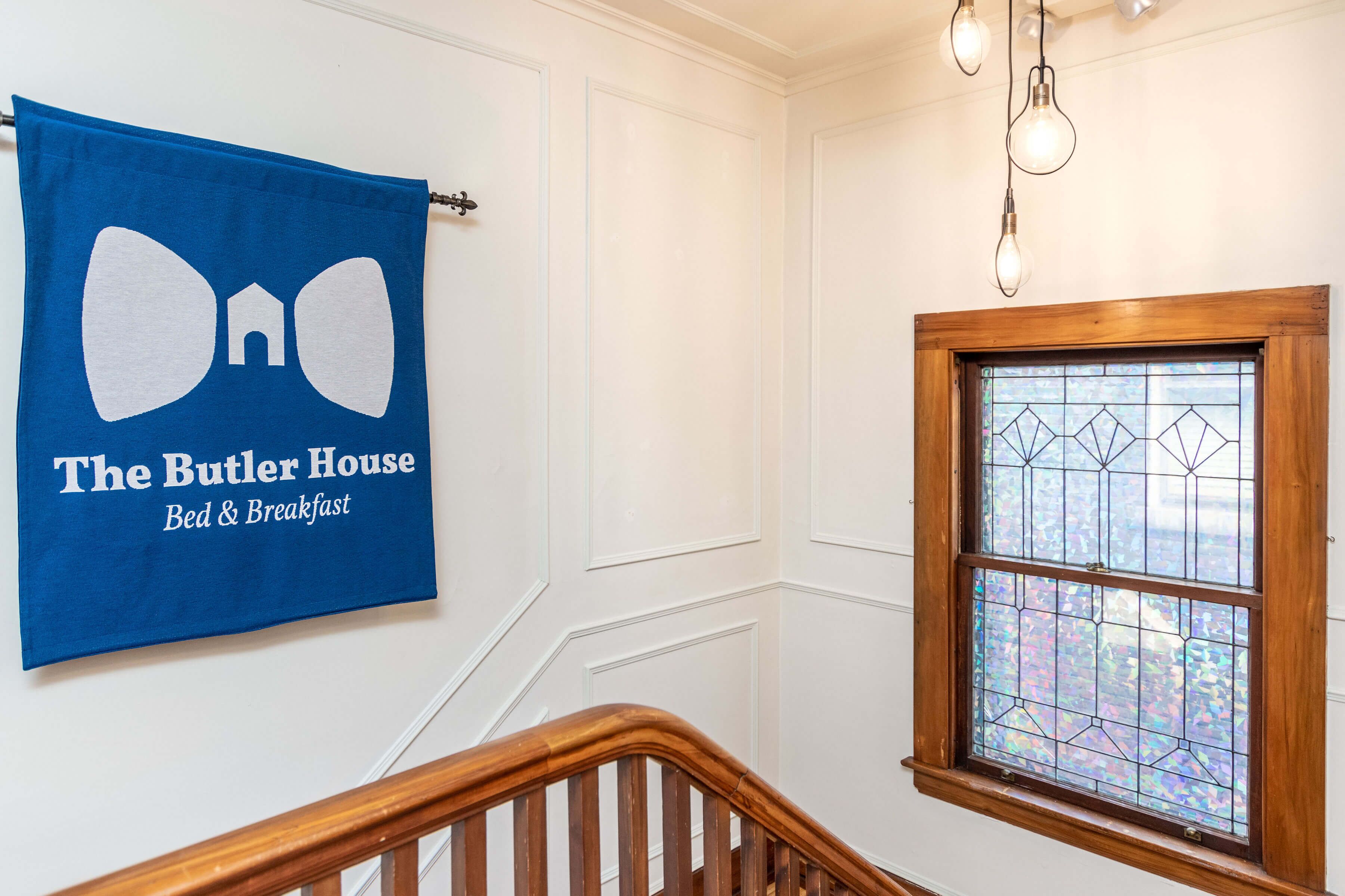 A blue towel with "The Butler House Bed & Breakfast" text, a wooden staircase, and a stained glass window.