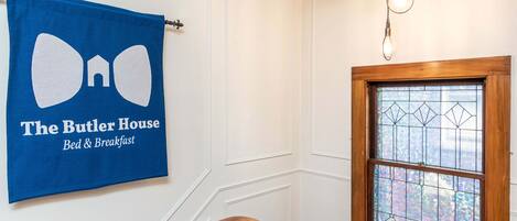 A blue towel with "The Butler House Bed & Breakfast" text, a wooden staircase, and a stained glass window.