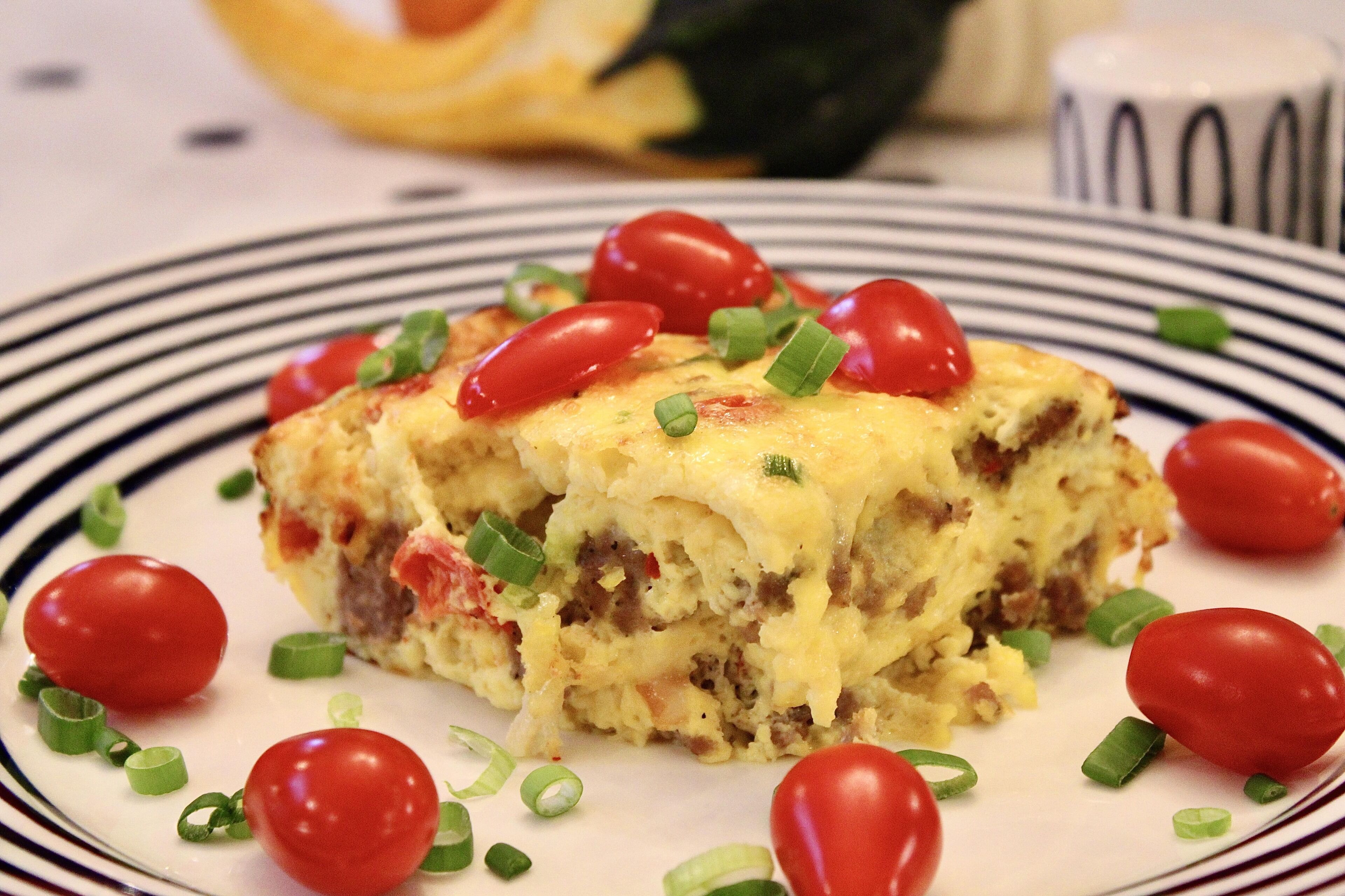 Una porción de quiche sobre un plato a rayas, con tomates cherry y cebollas verdes.