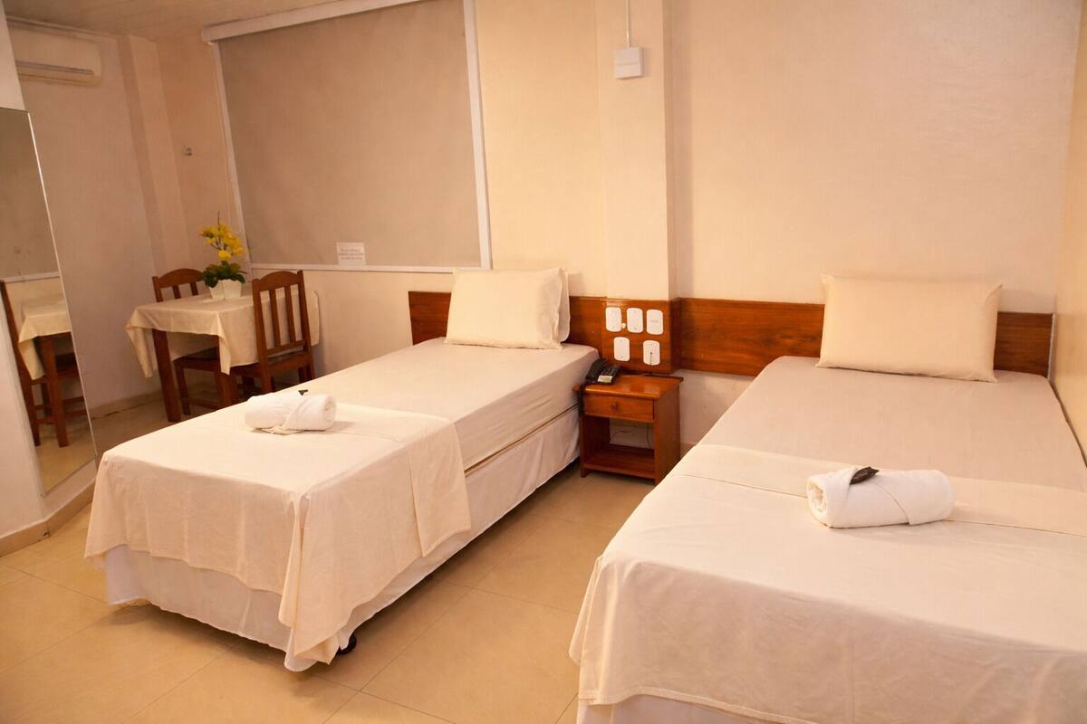 Une chambre d’hôtel avec deux lits, une petite table, une chaise et un miroir.