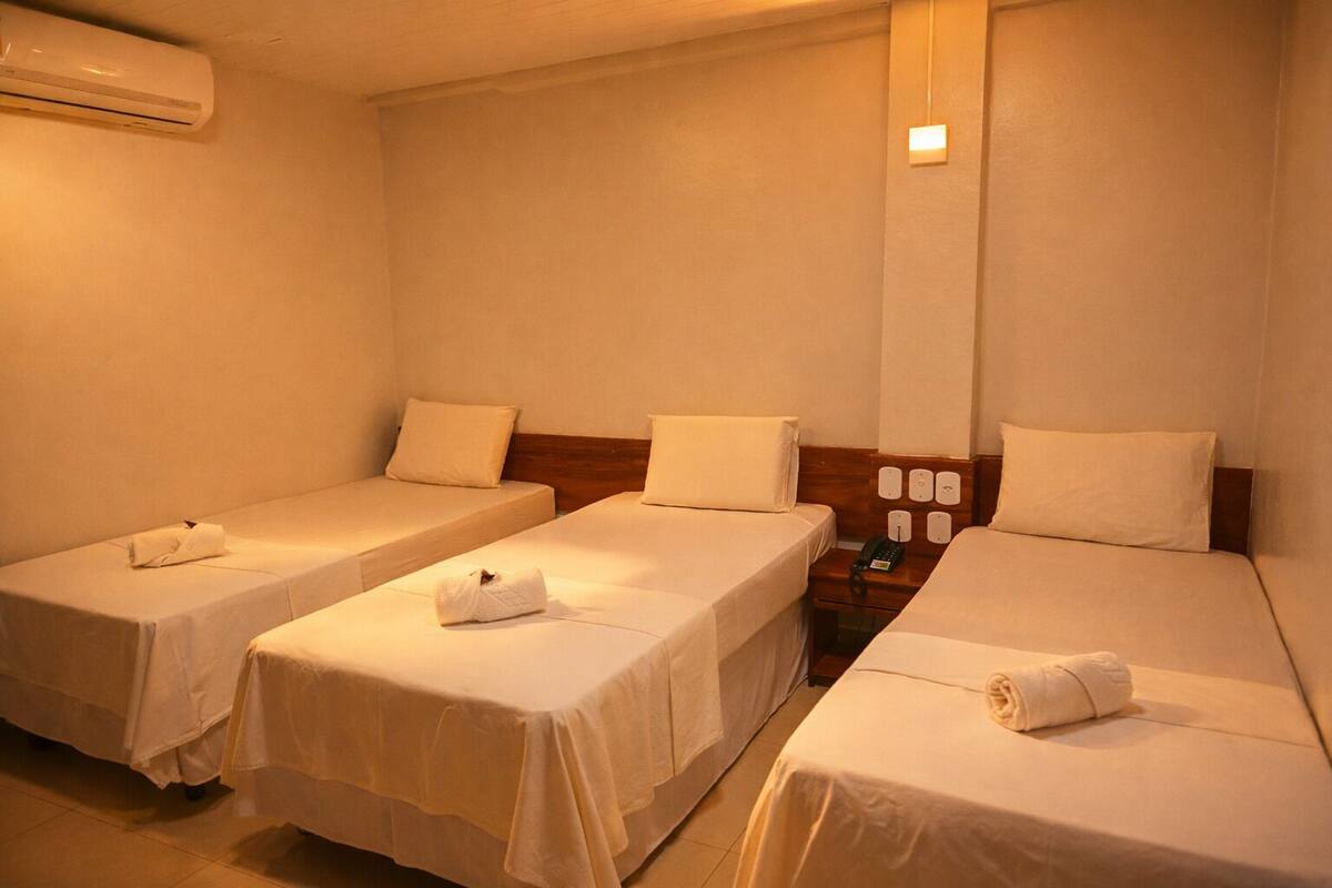 Une chambre d’hôtel avec trois lits simples, une table de chevet avec un téléphone et un appareil de climatisation.