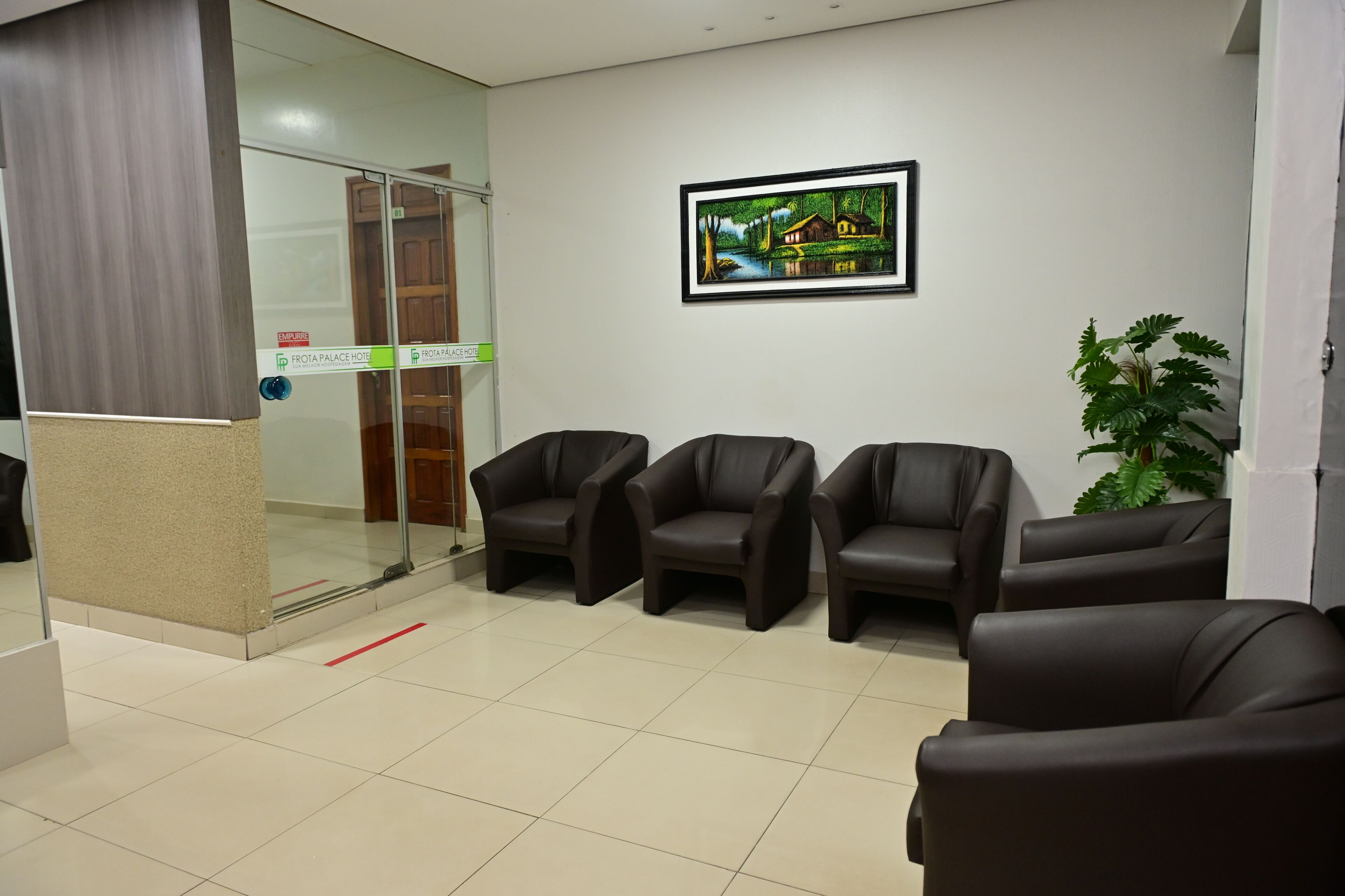 Un área de recepción con puerta de vidrio, un cuadro en la pared y varias sillas de cuero.