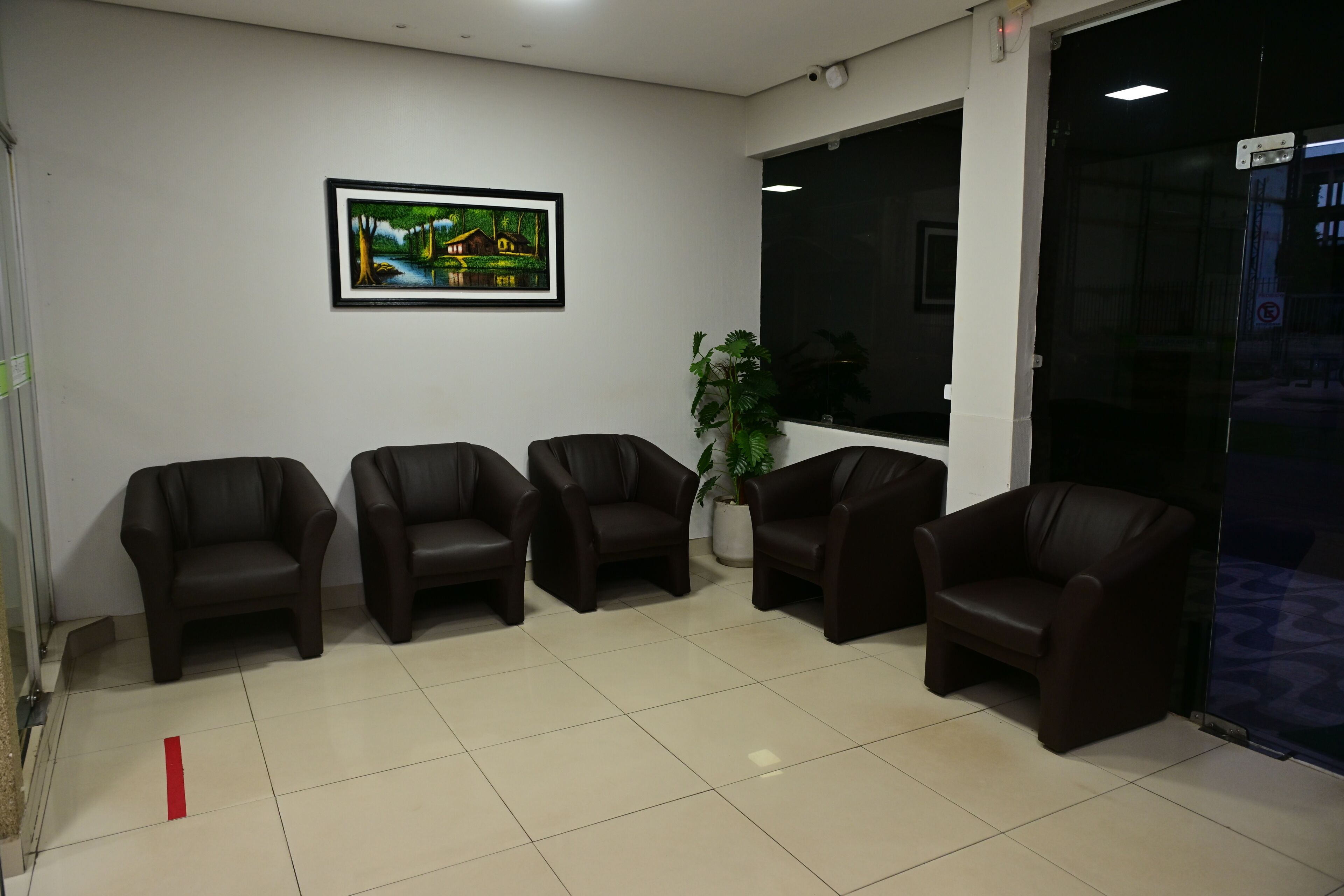 A waiting area with five leather chairs, a framed painting, and a potted plant.
