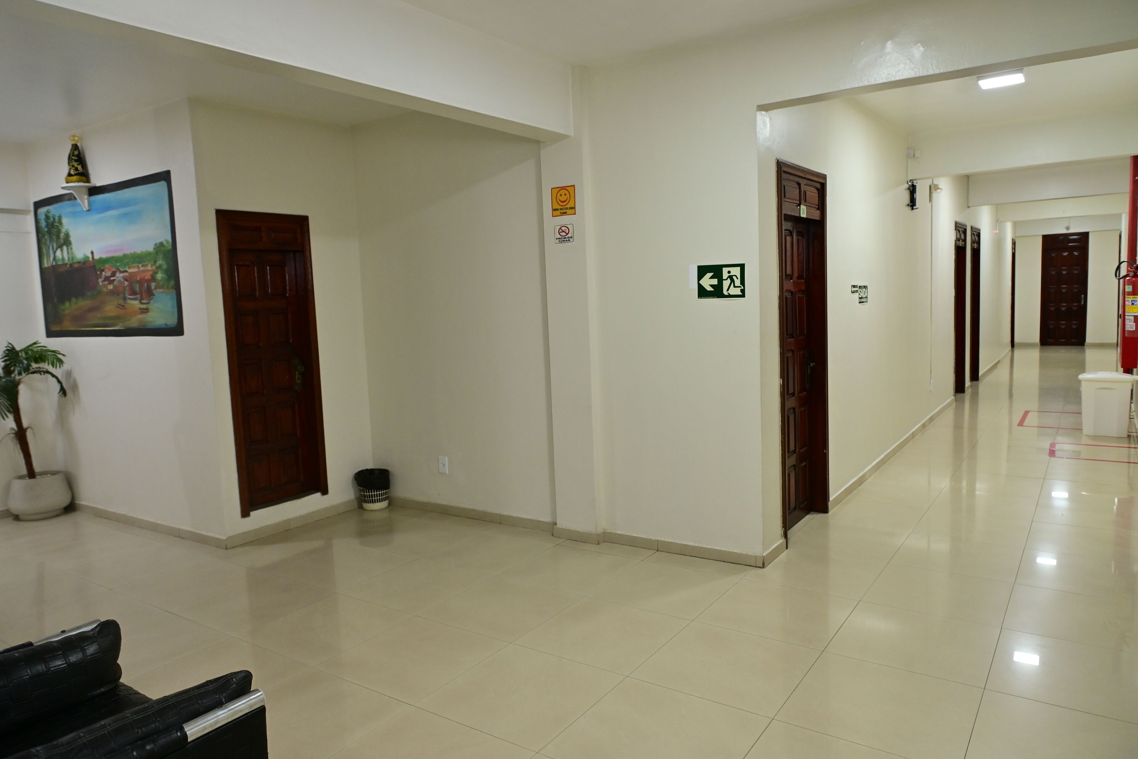 Una hall d'albergo con pavimento piastrellato, porte in legno, una pianta in vaso, una panca e un quadro appeso al muro.
