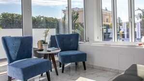 Une pièce avec deux fauteuils bleus, une petite table ronde et une grande fenêtre donnant sur des immeubles et des arbres.