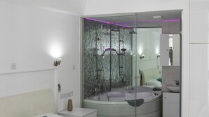 Une chambre moderne comprenant un lit, un ventilateur de plafond, un appareil de climatisation, une douche séparée par des parois en verre, et une salle de bain avec un lavabo et un miroir.