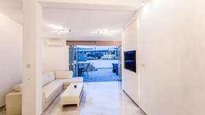 Un salon moderne avec un canapé, une table basse et un téléviseur. Il y a un balcon équipé de mobilier d’extérieur.