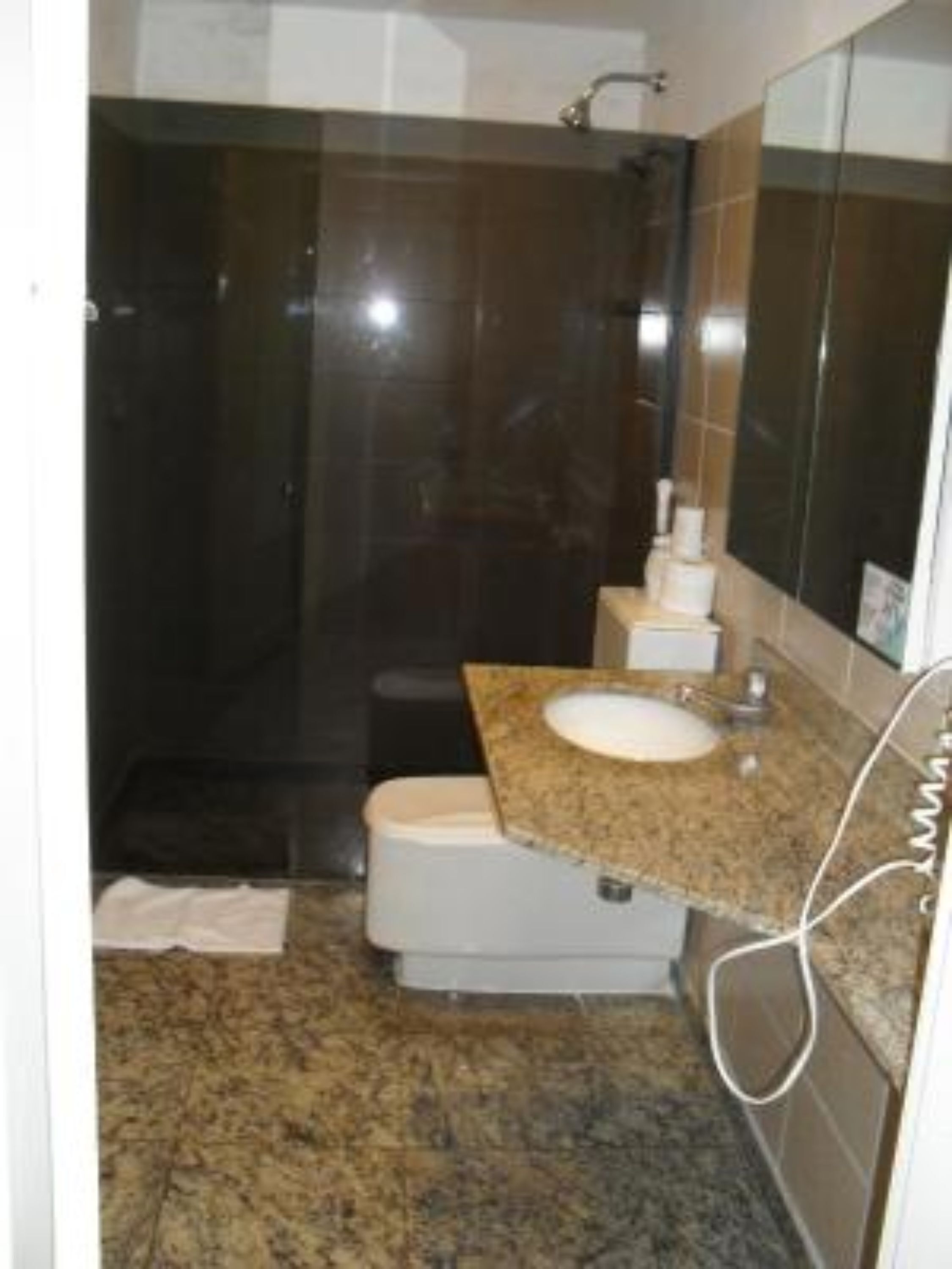 A bathroom with a dark shower, a sink with a granite countertop, and a mirror.