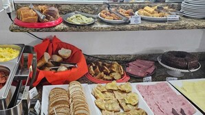 A buffet with various food items including scrambled eggs, sausages, bread, and different types of cheese. - Hotel Dublin (São Paulo)