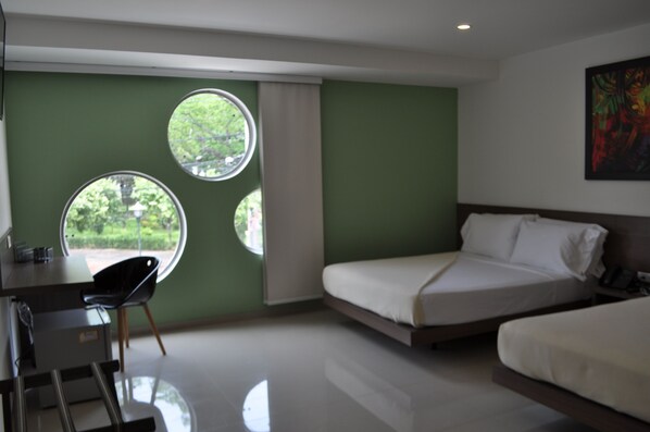 A hotel room with a bed, a desk, and two windows.