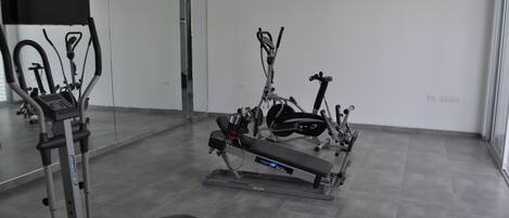 Uma academia com máquinas de cardio, um banco e um espelho grande na parede.