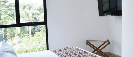 Una habitación de hotel con un ventanal grande, una cama con ropa blanca, un colcha colorida y un televisor montado.