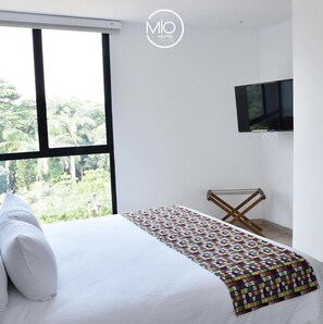 A hotel room with a large window, a bed with white bedding, a colorful quilt, and a mounted TV. - Hotel Mio Boutique (San José de Cúcuta)