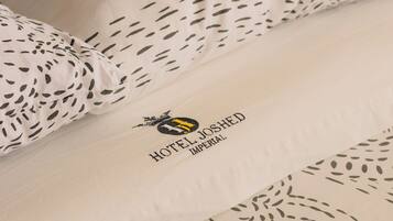 A hotel bed with a logo and name "HOTEL JOSHED IMPERIAL" on the pillowcase.