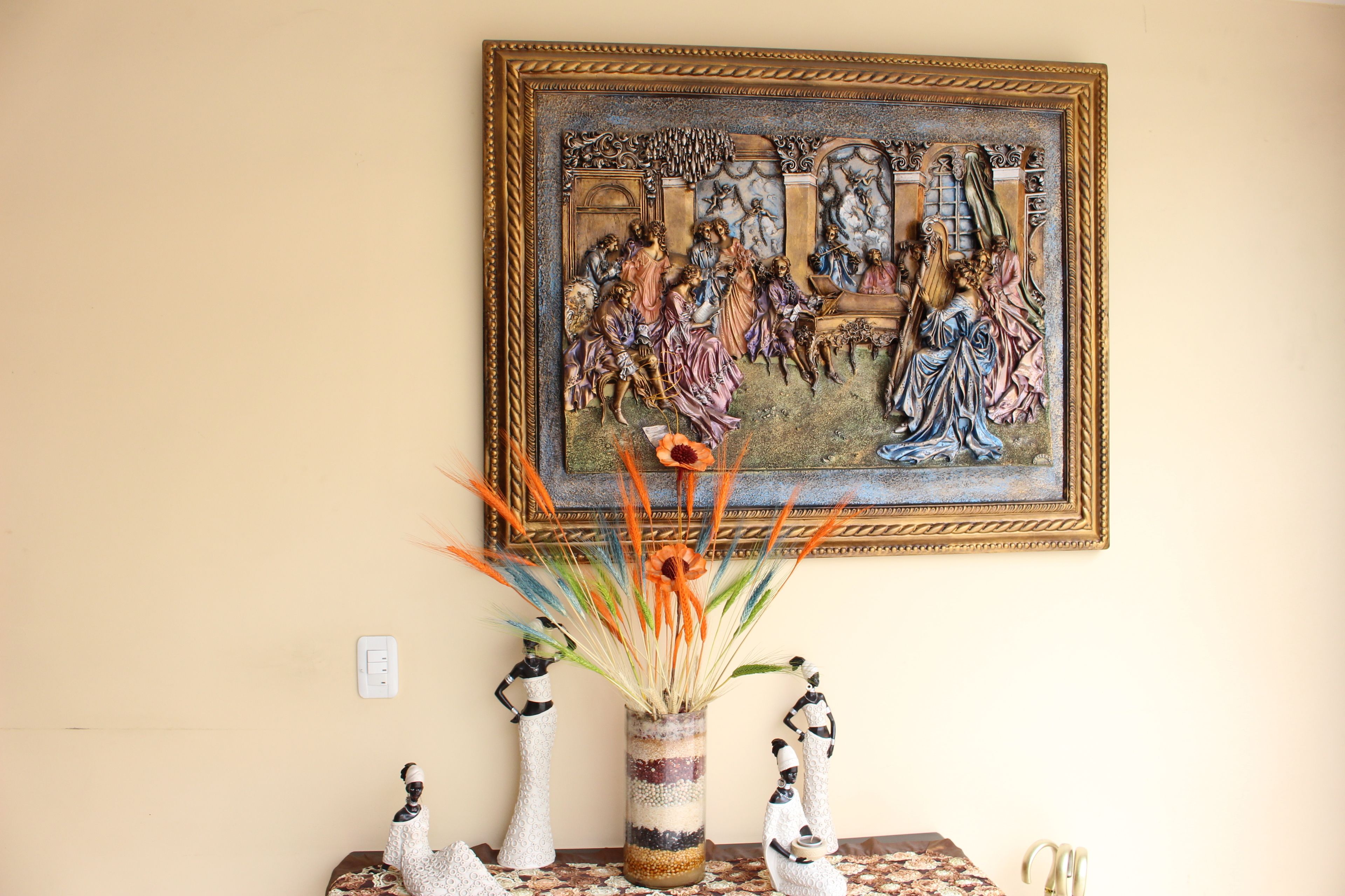Una stanza con un quadro appeso al muro, un vaso con piante essiccate e figure decorative su un tavolo.