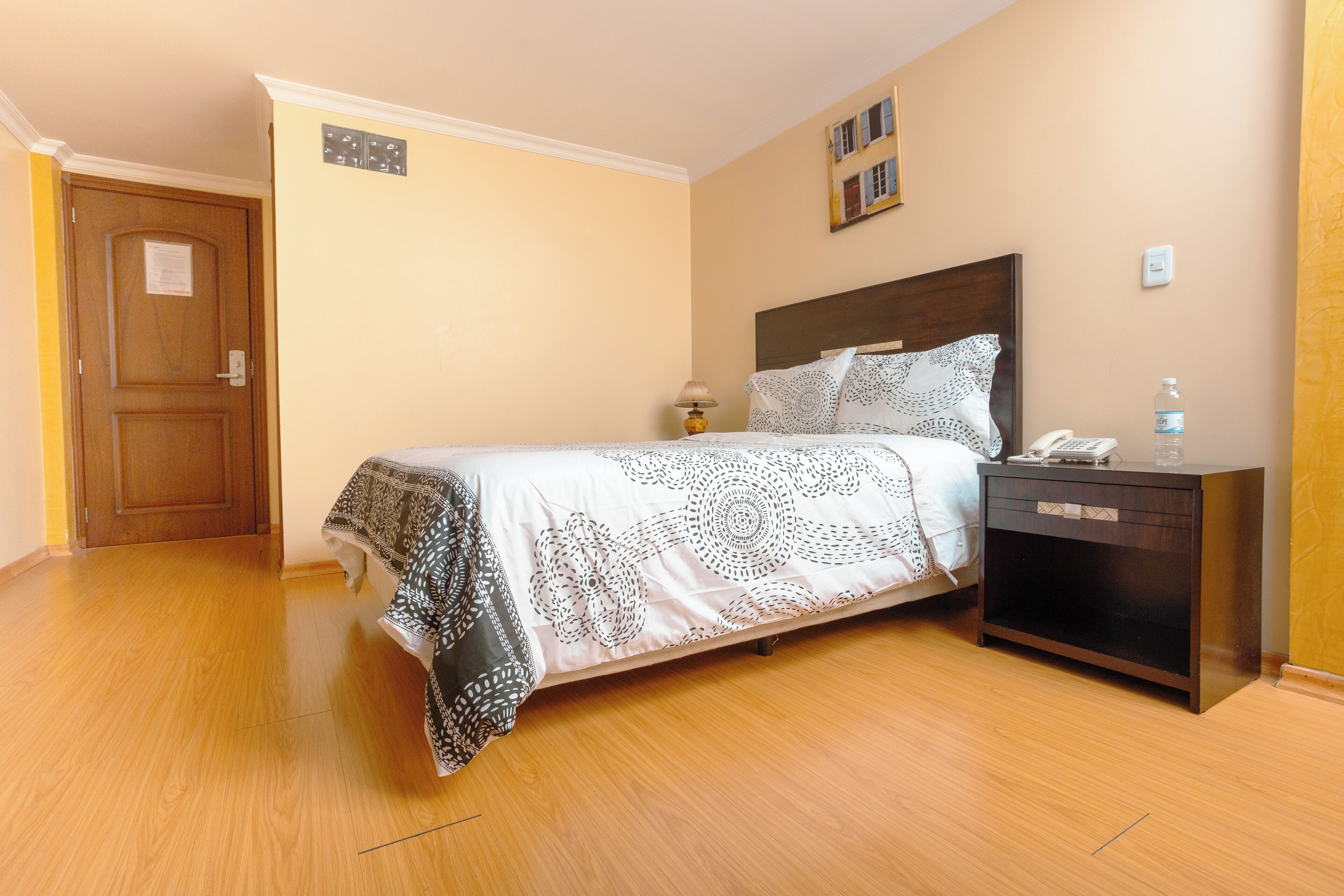 Un dormitorio con cama, mesita de noche, lámpara y teléfono instalado en la pared.