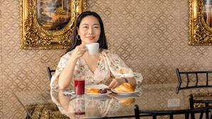 Une personne assise à une table, devant un verre de jus de fruits, une assiette de nourriture et une tasse.