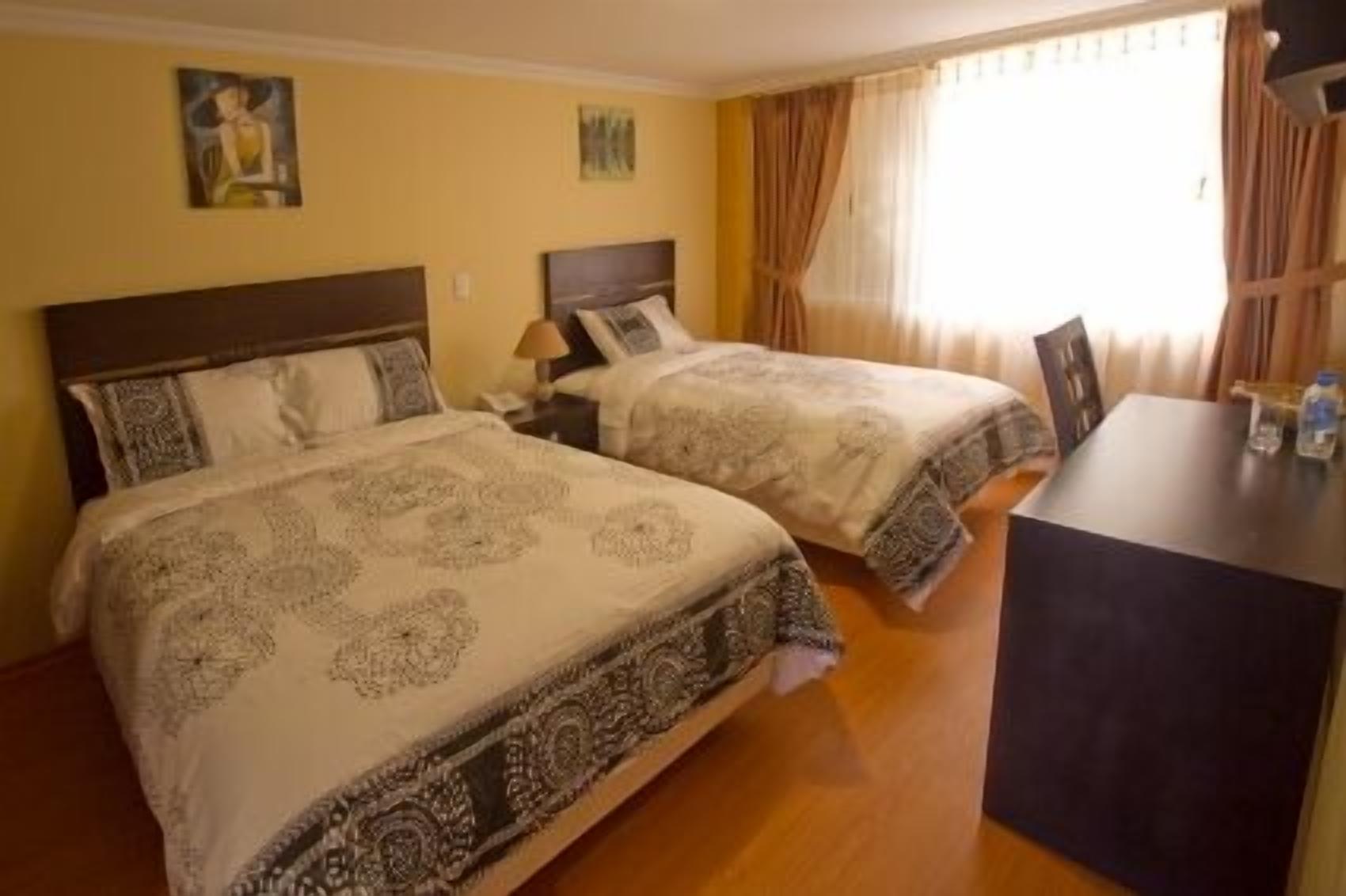 Une chambre d’hôtel avec deux lits, un bureau et une fenêtre avec des rideaux.