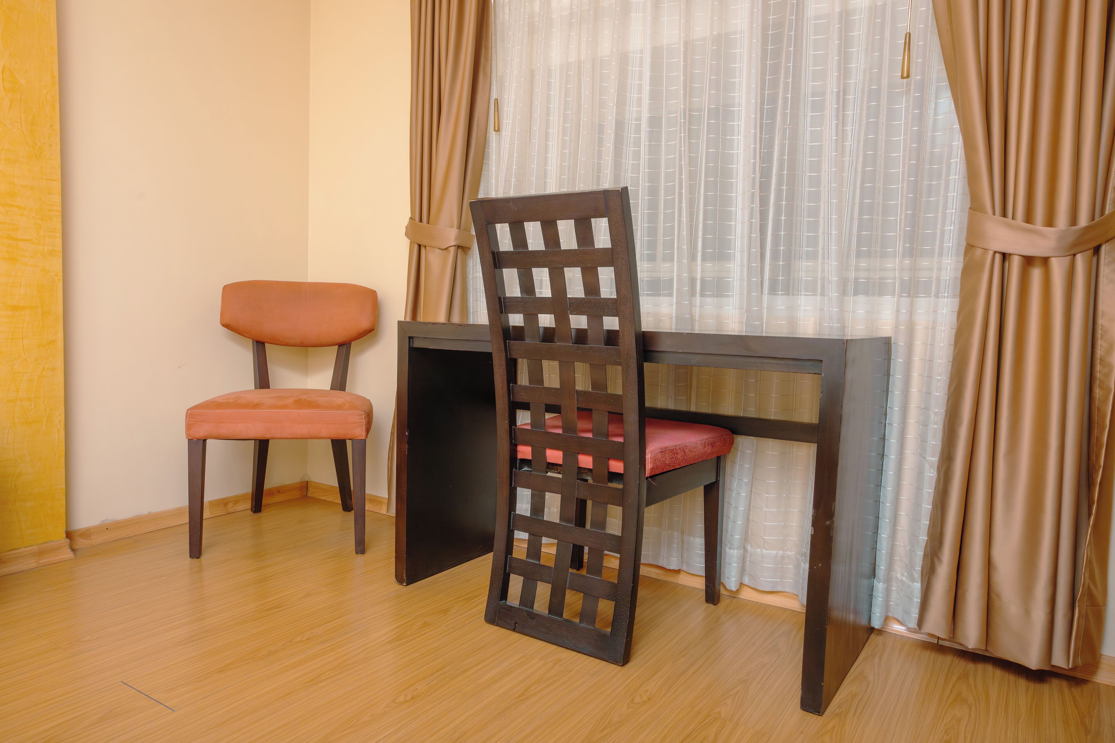 A room with a wooden desk, two chairs, and a window with curtains.