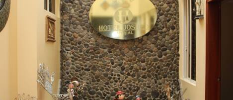 Ein Empfangsbereich mit Steinwand, einem Schild mit der Aufschrift 'HOTEL JOSHEP' und Dekorationselementen, darunter ein Pfau und Figuren.