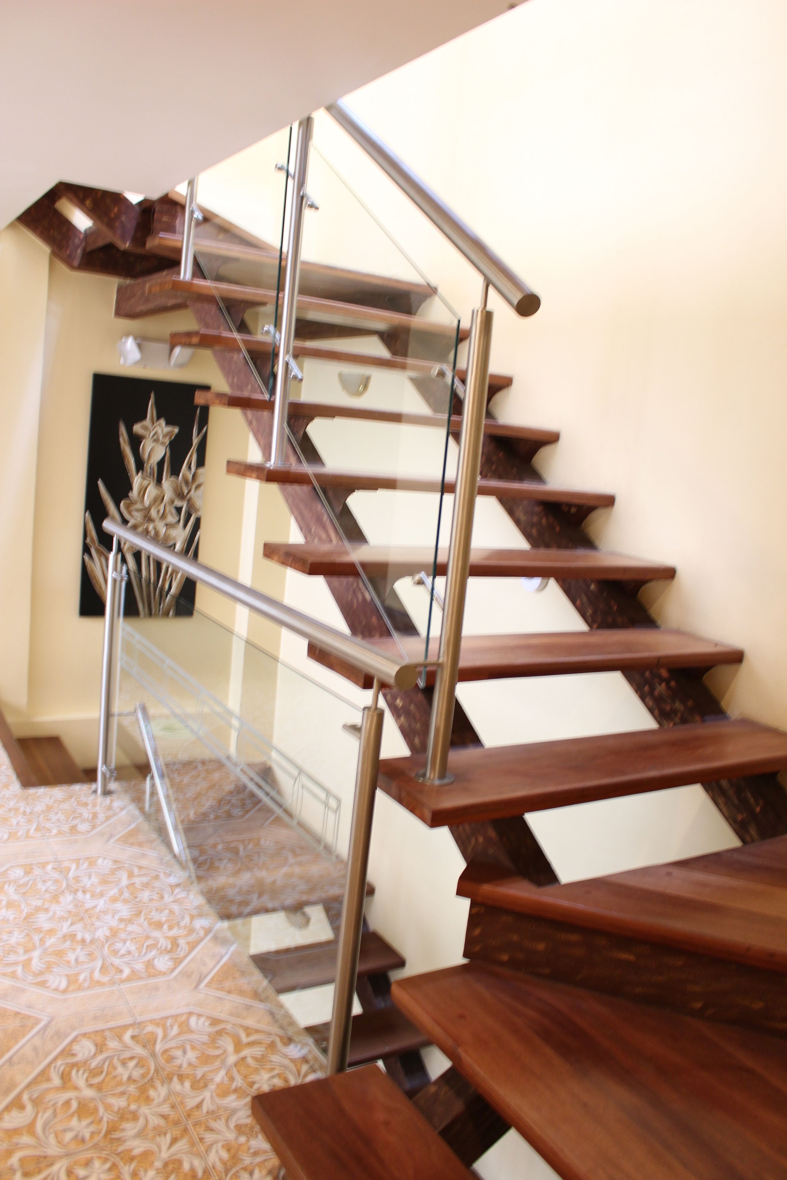 A wooden staircase with glass railings and a patterned floor.