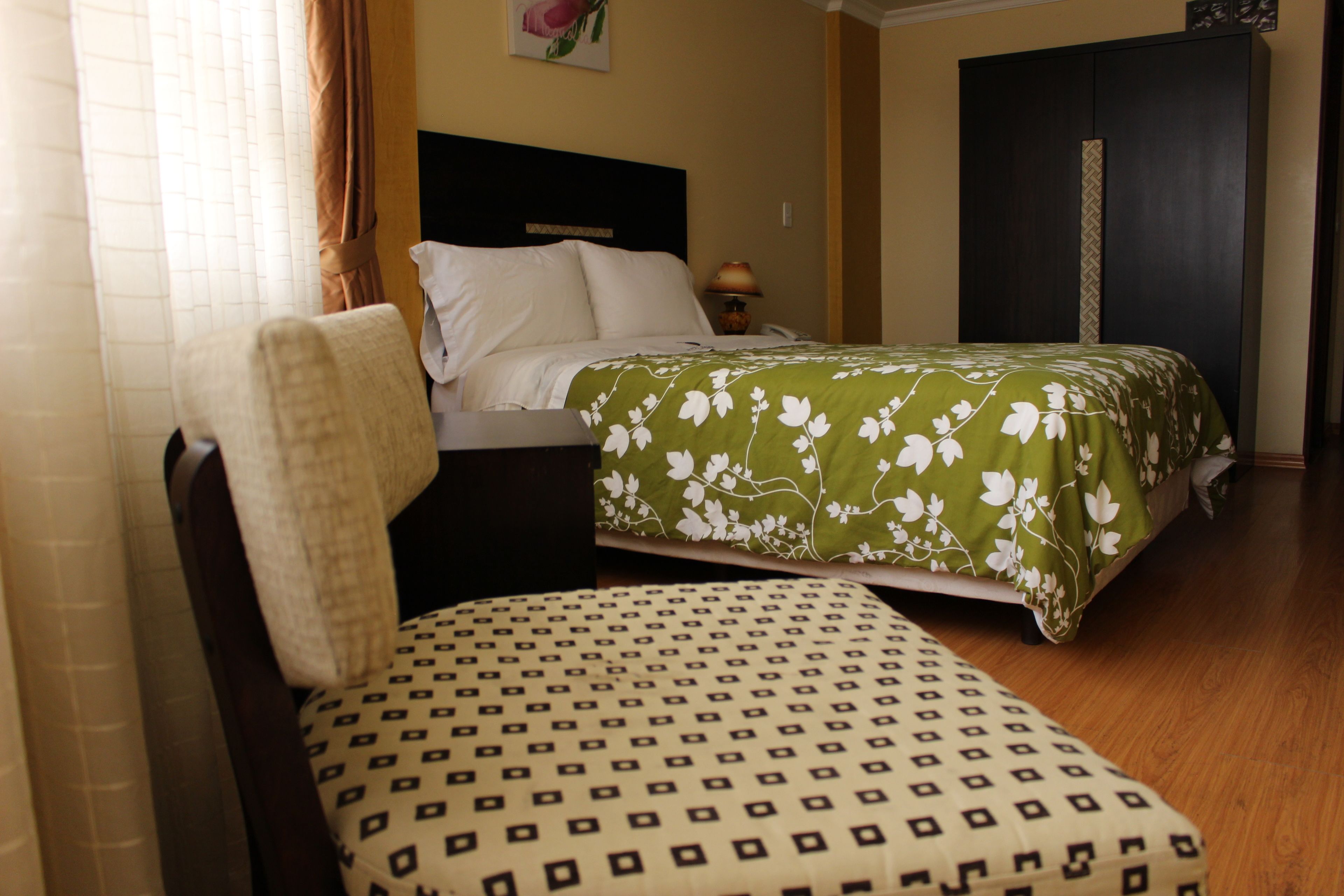 A hotel room with a bed, a chair, a nightstand, and a wardrobe.