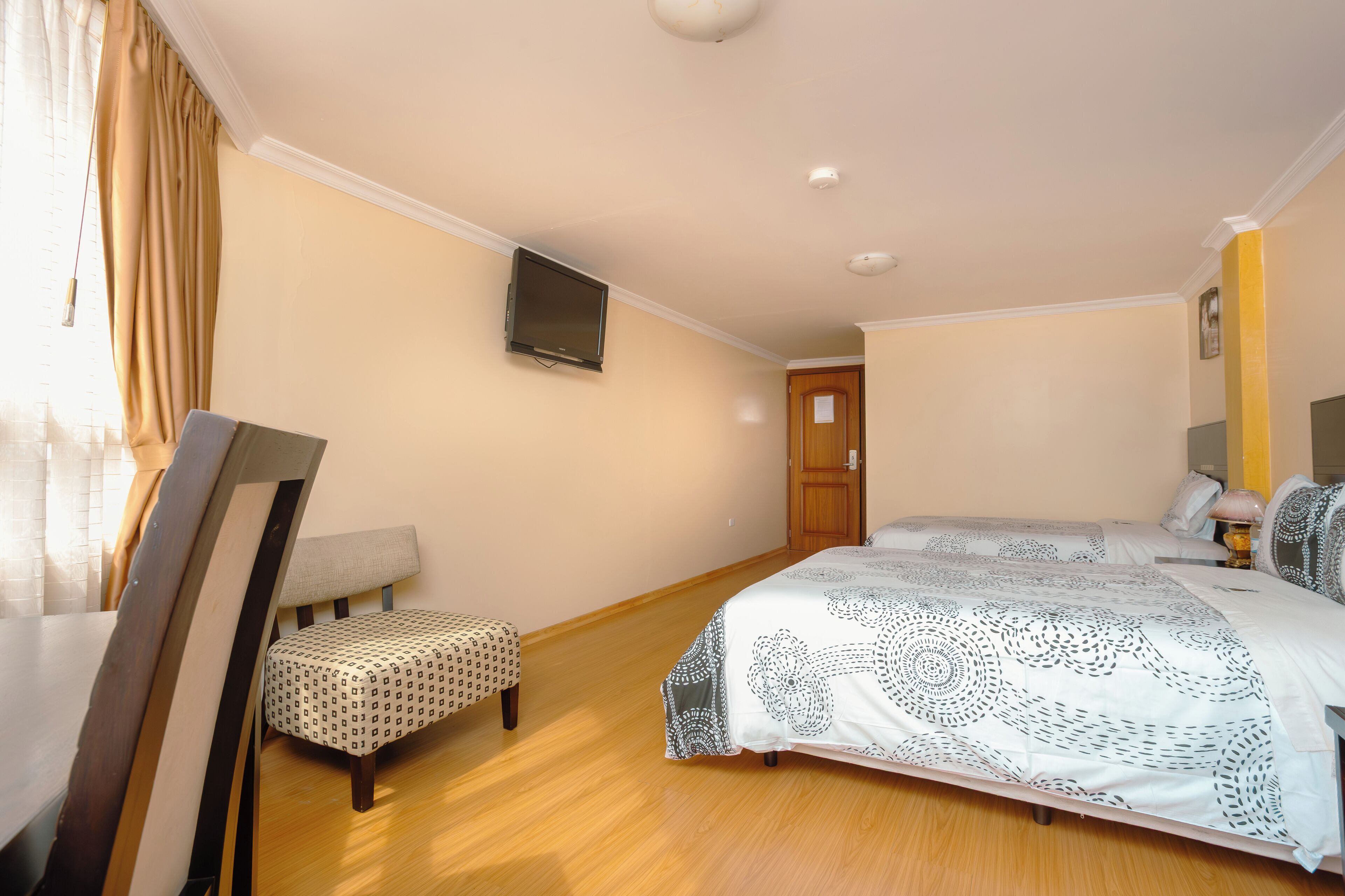A hotel room with a bed, a chair, a television, and a wooden floor.