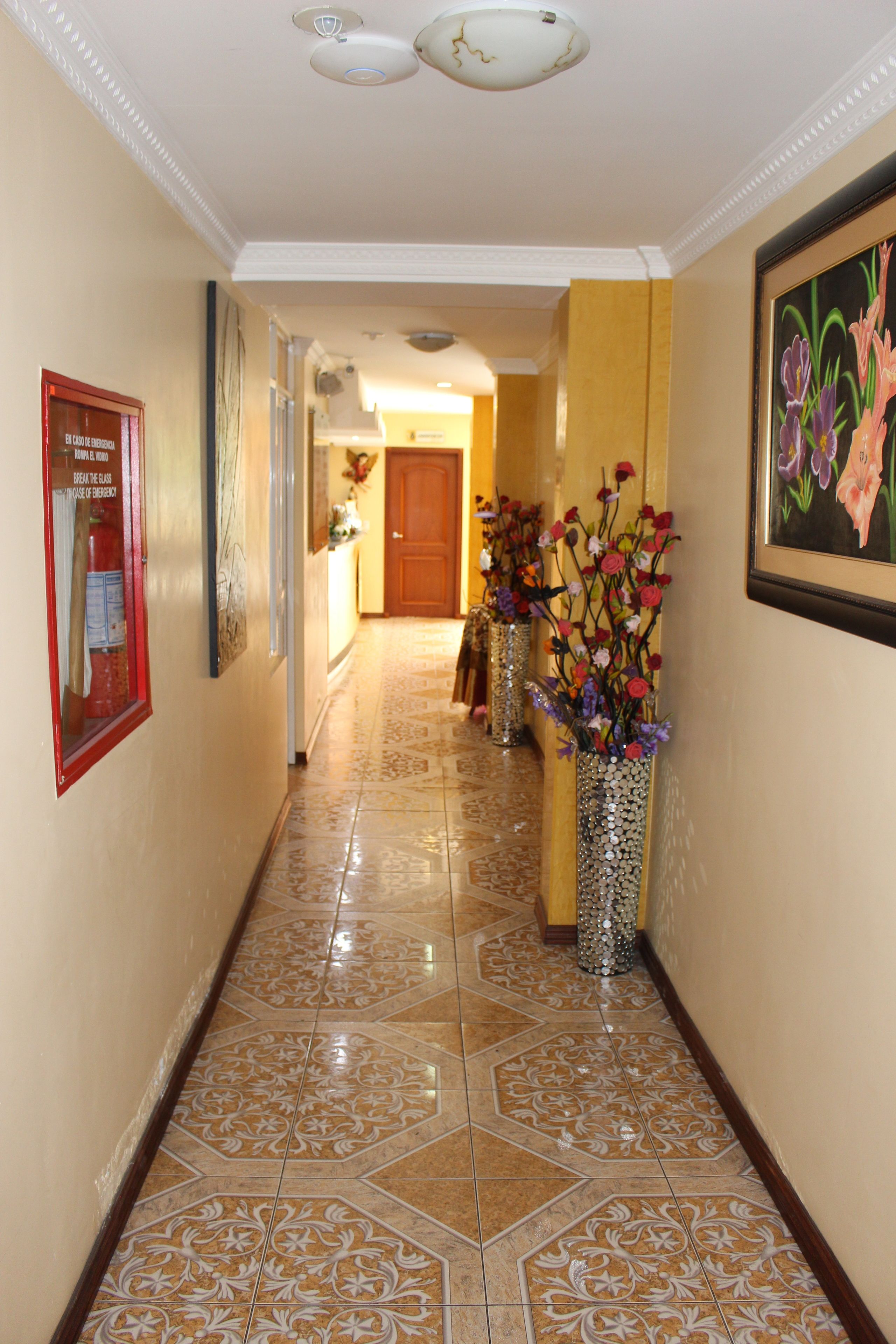 A hallway with patterned tile flooring, decorative vases with flowers, and framed artwork on the walls.