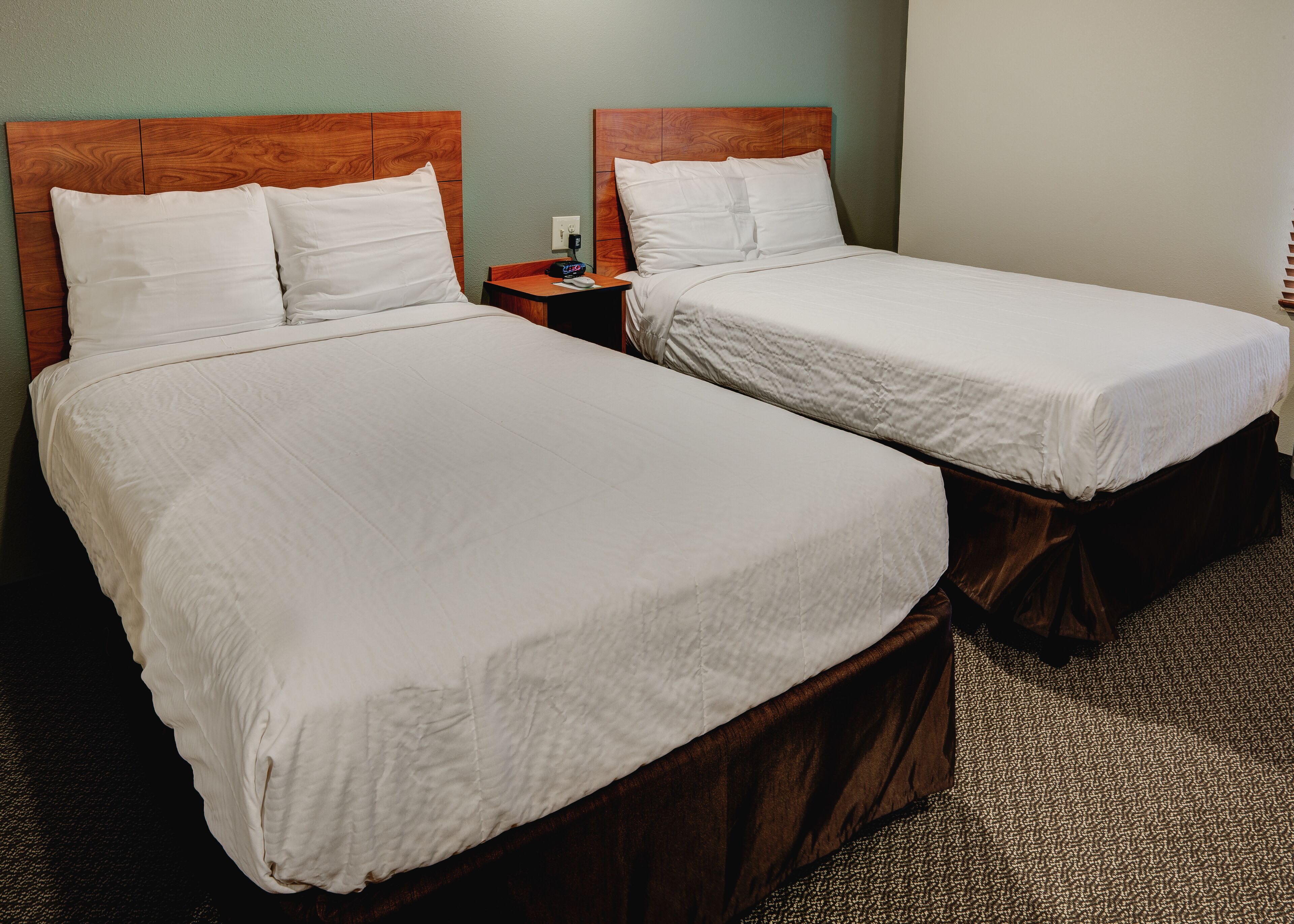 Two single beds with wooden headboards, white linens, and a small wooden nightstand with a phone and a power outlet between them.
