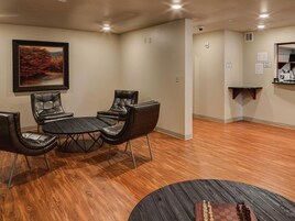 Una habitación con piso de madera, una mesa con cuatro sillas, un tablero de ajedrez y un cuadro en la pared.