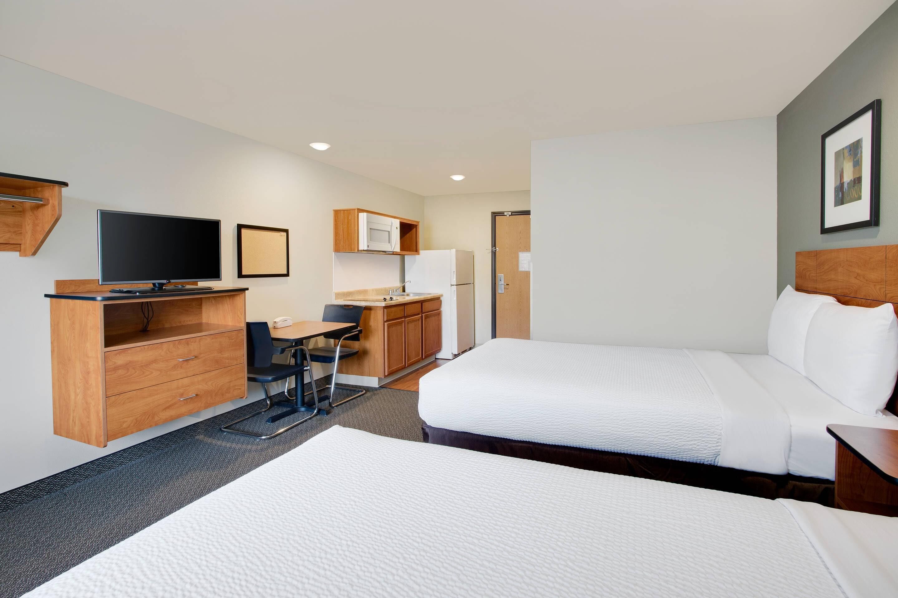 A hotel room with two beds, a desk, a television, a microwave, and a refrigerator.