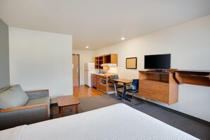 A hotel room with a bed, a desk, a chair, a television, and a kitchenette. - WoodSpring Suites Columbus NE I-270 Airport (Columbus)