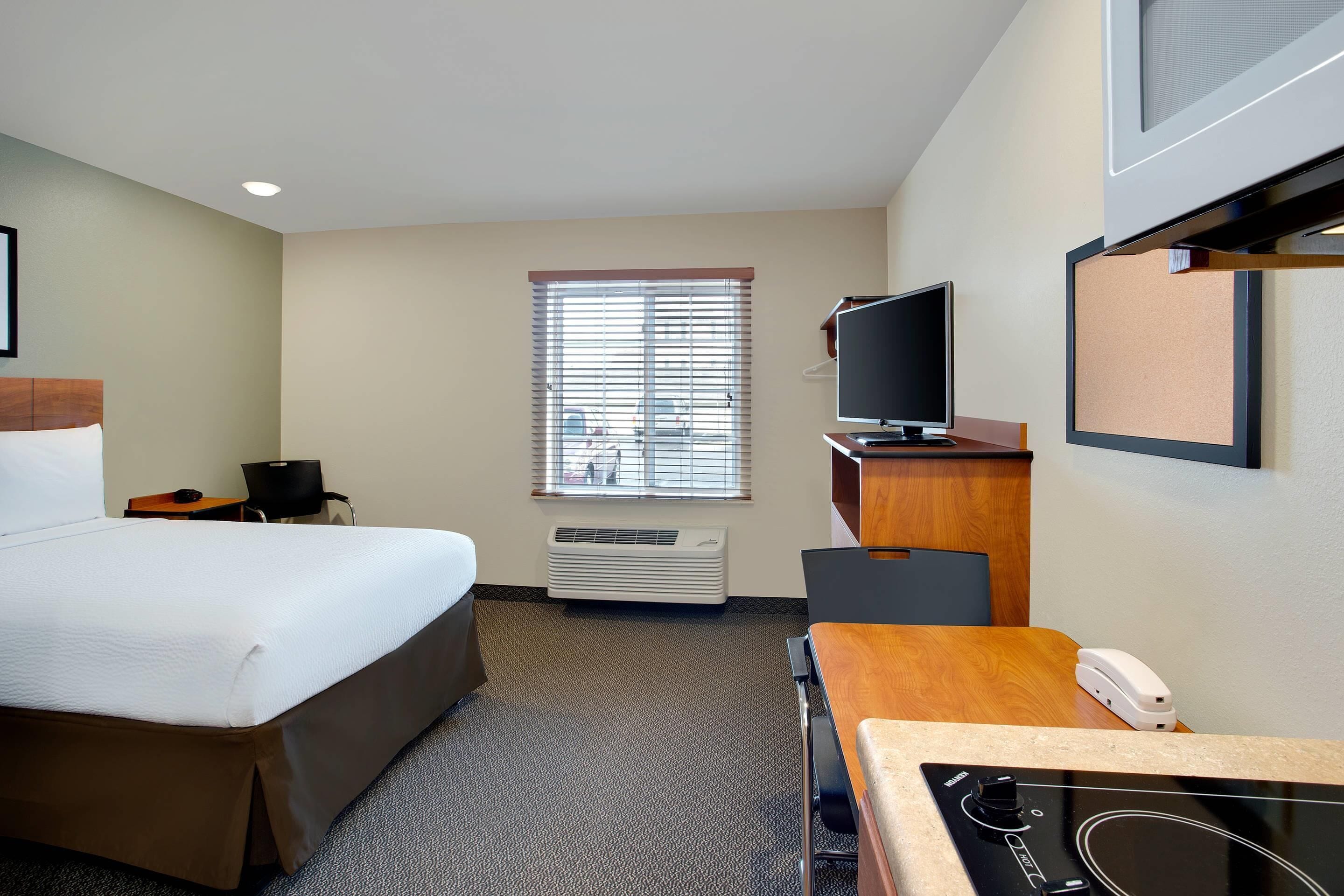 Una habitación de hotel con cama, escritorio con computadora, televisor y aire acondicionado.