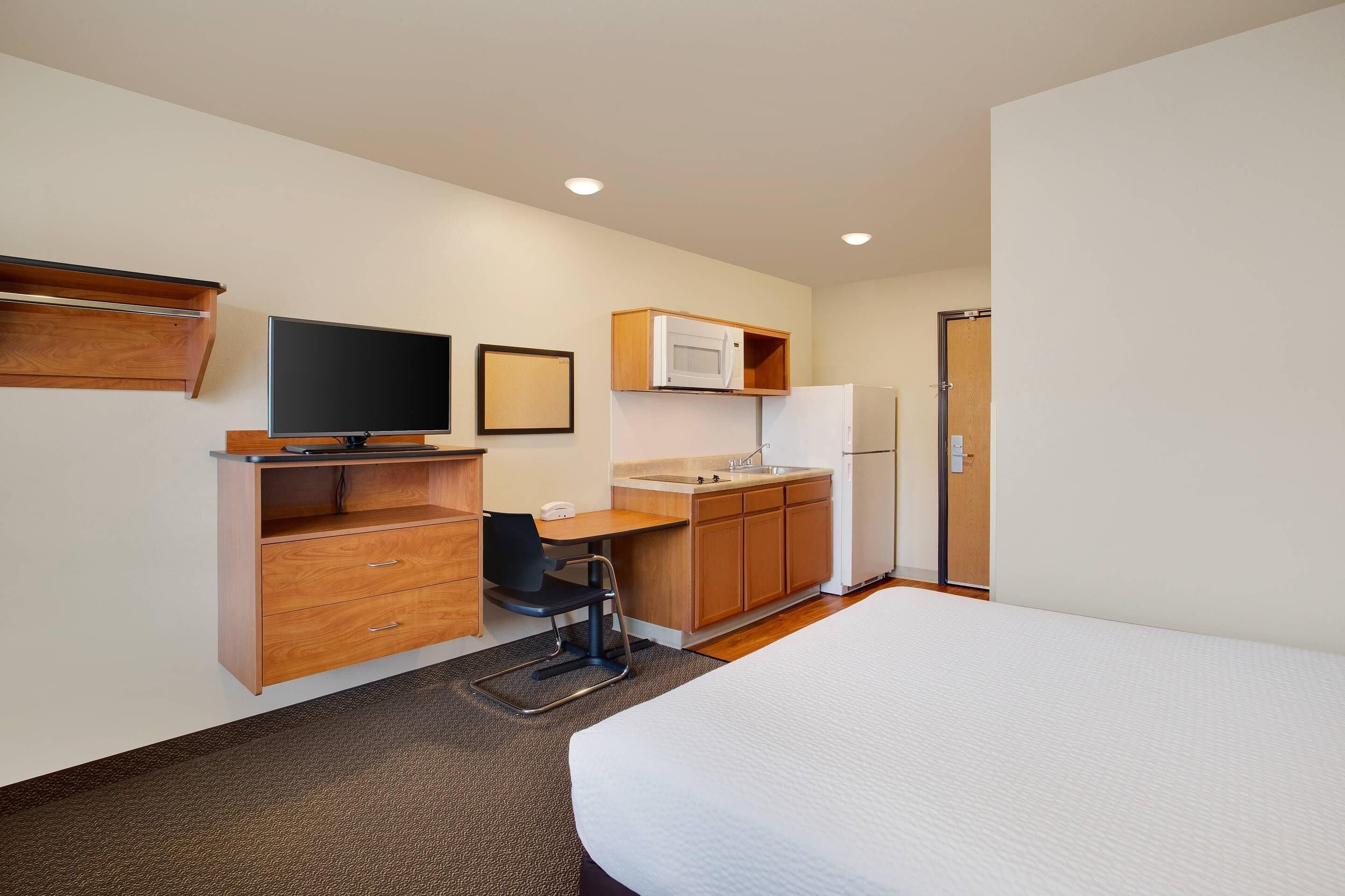 A hotel room with a bed, a desk with a chair, a television, a microwave, and a refrigerator.