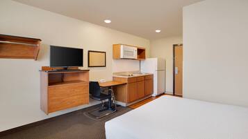 Habitación de hotel con cama, escritorio y silla, televisión, microondas y refrigerador.