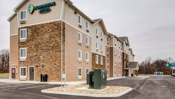 Un hôtel à plusieurs étages, doté d’une façade en pierre et d’une enseigne indiquant « Woodspring Suites ».