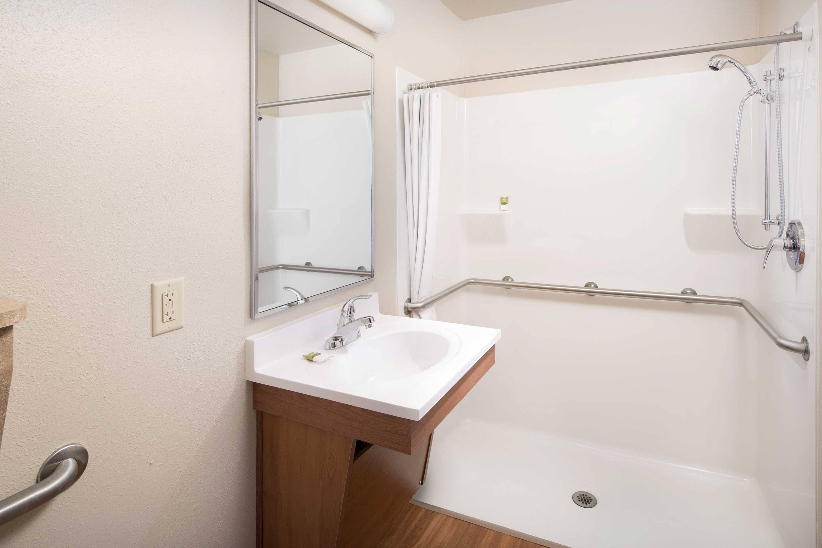 A bathroom with a white sink, mirror, and shower with grab bars.