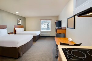 A hotel room with two beds, a desk, a TV, and a kitchenette.