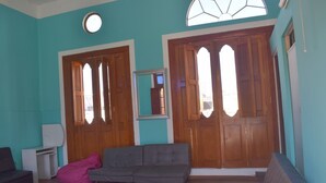 A room with teal walls, a wooden door with a mirror, a grey sofa, and a pink bean bag. - Mango Hostel Bed & Breakfast (Arequipa)