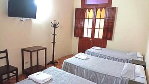 A hotel room with two beds, a TV, a coat rack, and a window with stained glass. - Mango Hostel Bed & Breakfast (Arequipa)
