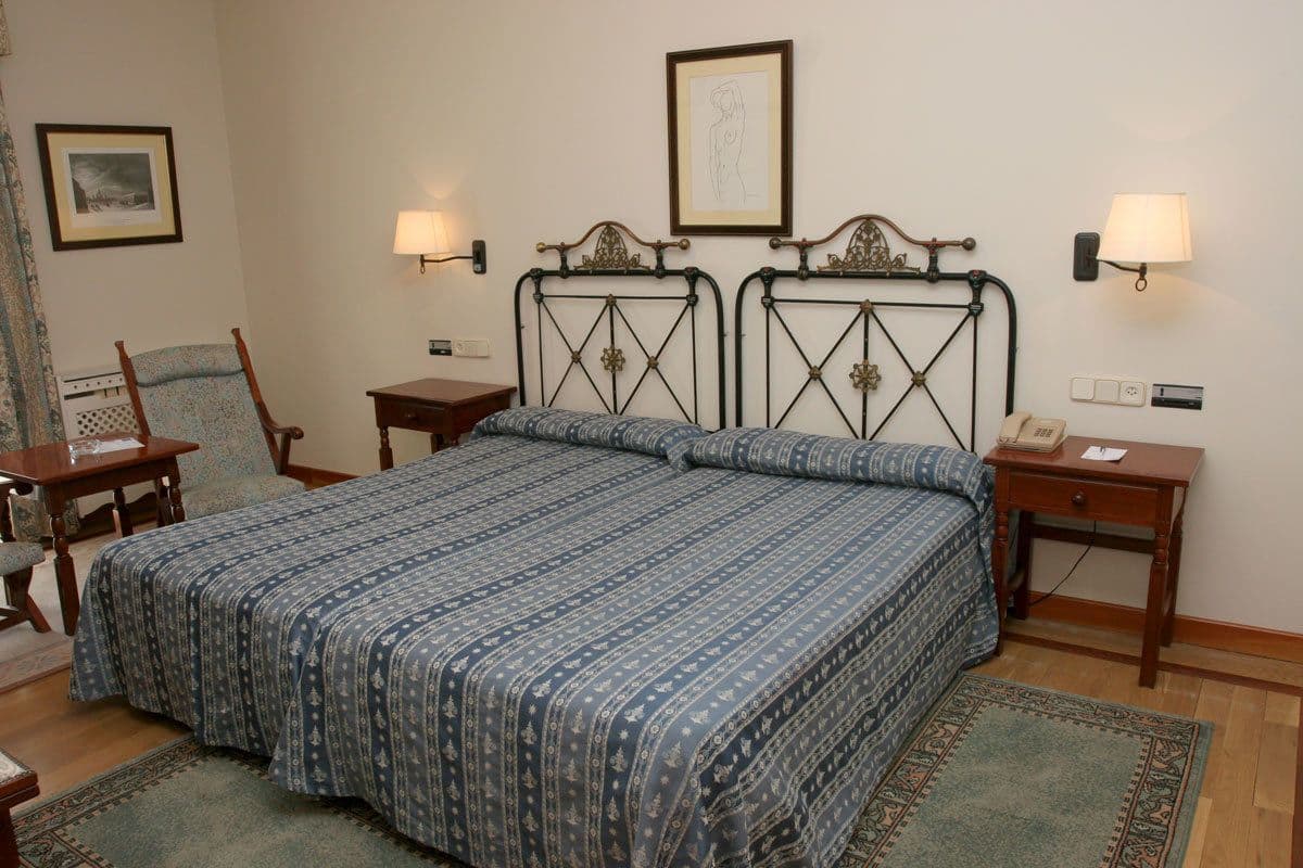 Un dormitorio con una cama grande, dos mesitas de noche, una silla, un escritorio y una lámpara.